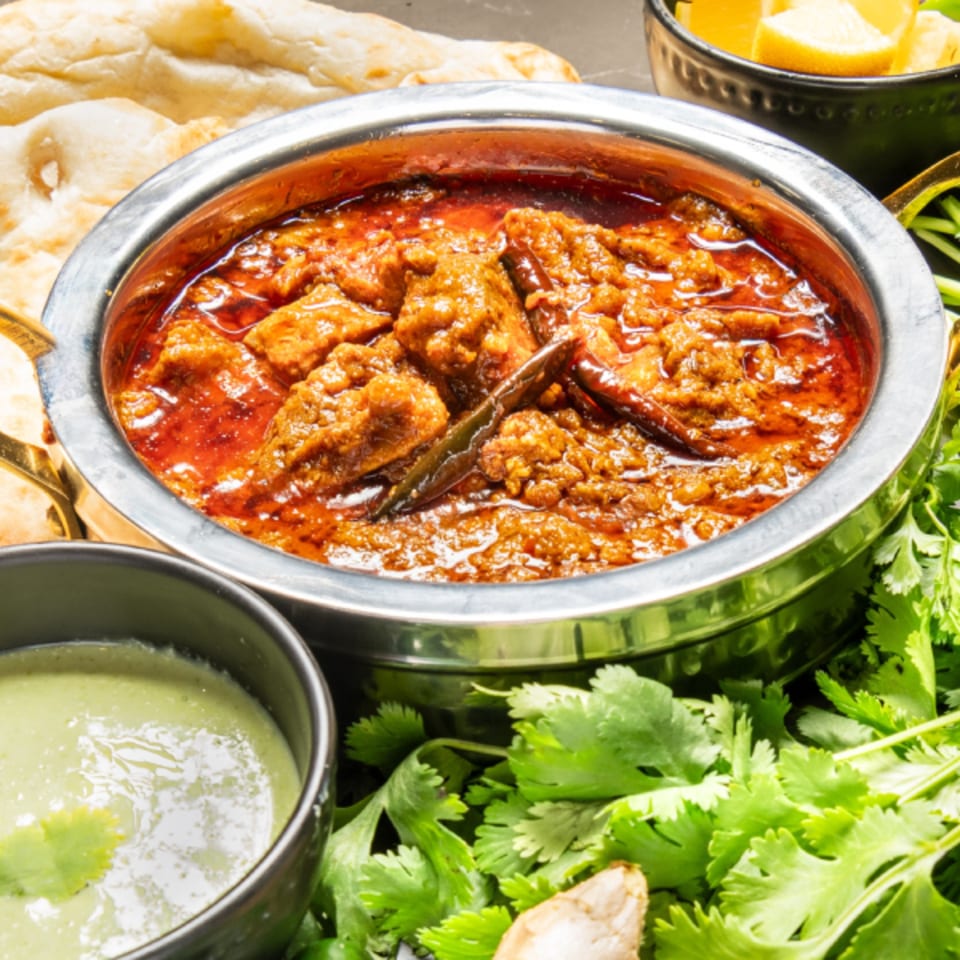 Pakistani karahi chicken in a metal bowl with naan, green chutney, and cilantro.