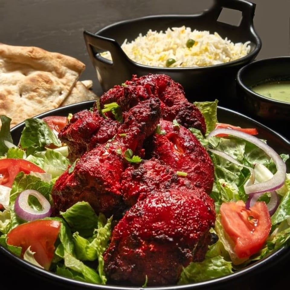 Pakistani tandoori chicken with salad, rice, naan, and green chutney on a dark background.