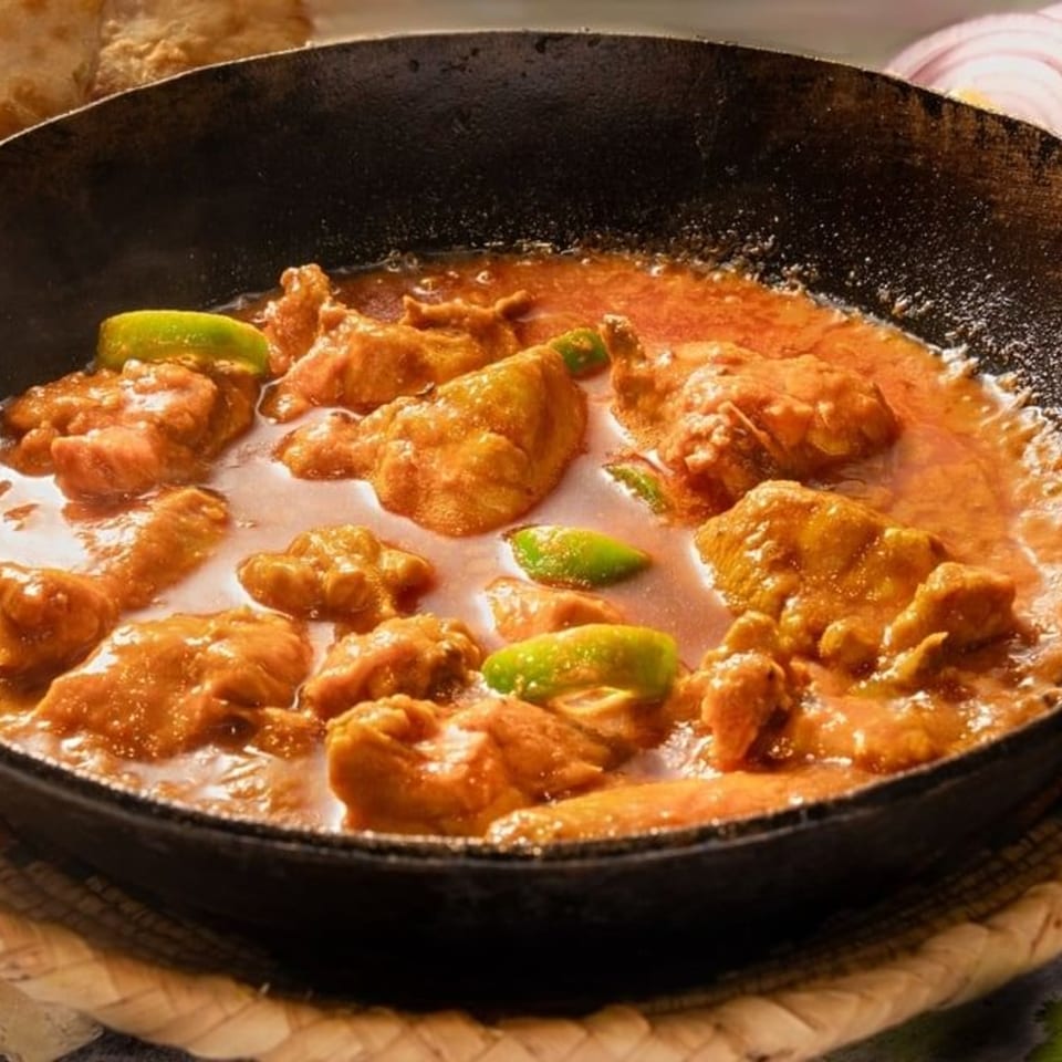 Pakistani chicken karahi, a rich orange curry with lime wedges, served in a black pan.