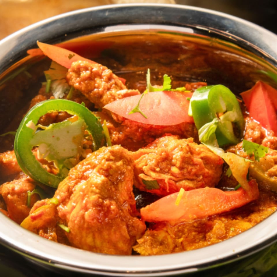 Close-up of Pakistani chicken karahi, garnished with sliced tomatoes, green chilies, and cilantro.