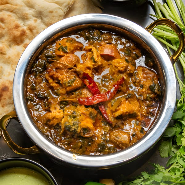 A close-up of Pakistani chicken karahi with red chilies, served with naan and green chutney.