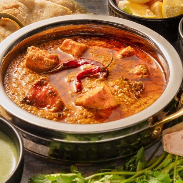 Pakistani chicken karahi in a metal bowl, with naan, lemon, and cilantro on the side.