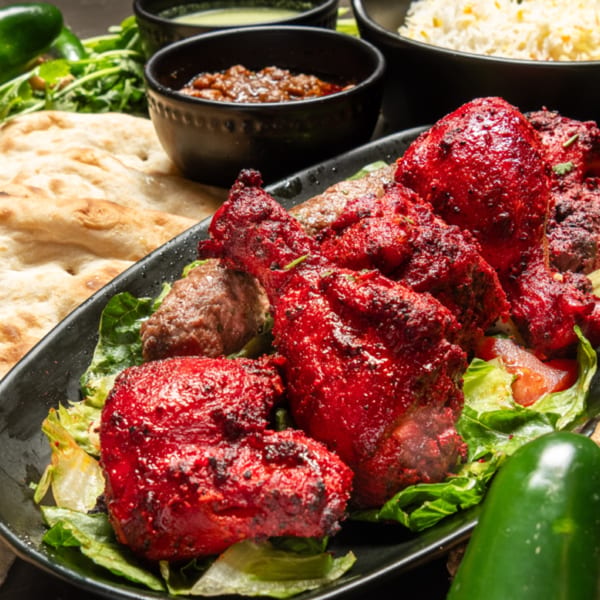Platter of vibrant red Pakistani chicken tikka and seekh kabobs with naan, rice, and sauces.