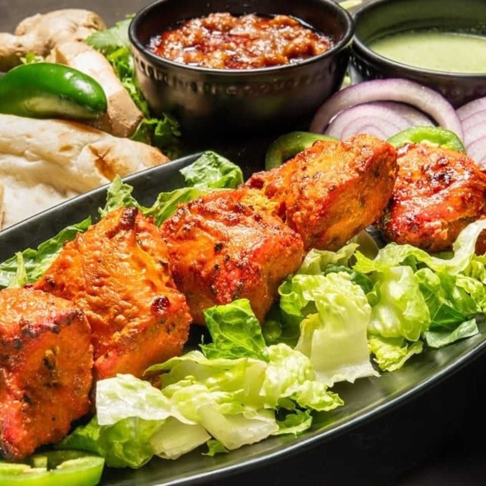 Pakistani chicken tikka on lettuce with sauces, naan, ginger, and onions.
