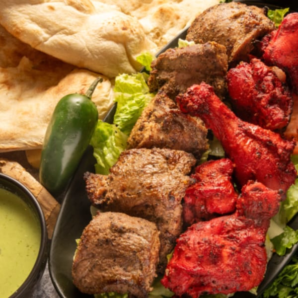 A platter of Pakistani food with red tandoori chicken, brown kabobs, naan bread, and green sauce.