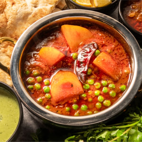 Aloo Matar, a Pakistani dish with potatoes and peas in a rich red sauce, served with naan.