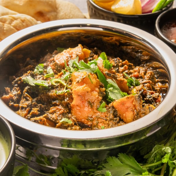 Close-up of a Pakistani chicken and spinach curry, garnished with fresh cilantro in a steel karahi.