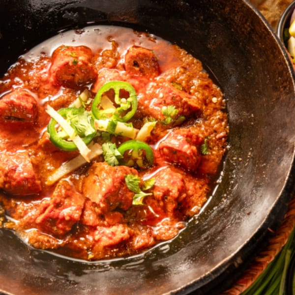 Pakistani karahi dish with meat, red sauce, green chilies, and cilantro in a black pan.