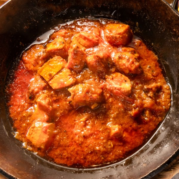 Close-up of a Pakistani chicken karahi dish with rich red sauce in a black pan.