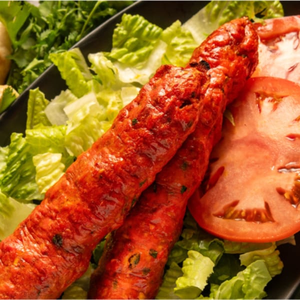 Two red Pakistani seekh kabobs on a bed of fresh lettuce with sliced tomatoes.