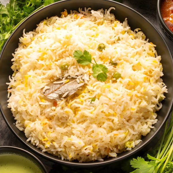 A black bowl filled with Pakistani pulao rice, garnished with cilantro and a bay leaf.