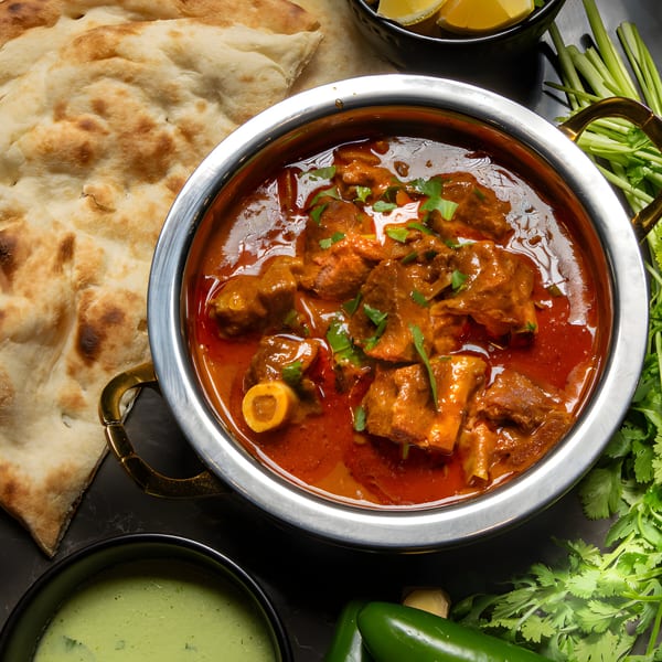 A Pakistani karahi dish with meat in a rich red sauce, served with naan bread and green chutney.