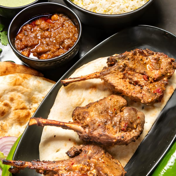 Pakistani lamb chops on naan bread with chickpea curry, rice, and green sauce.